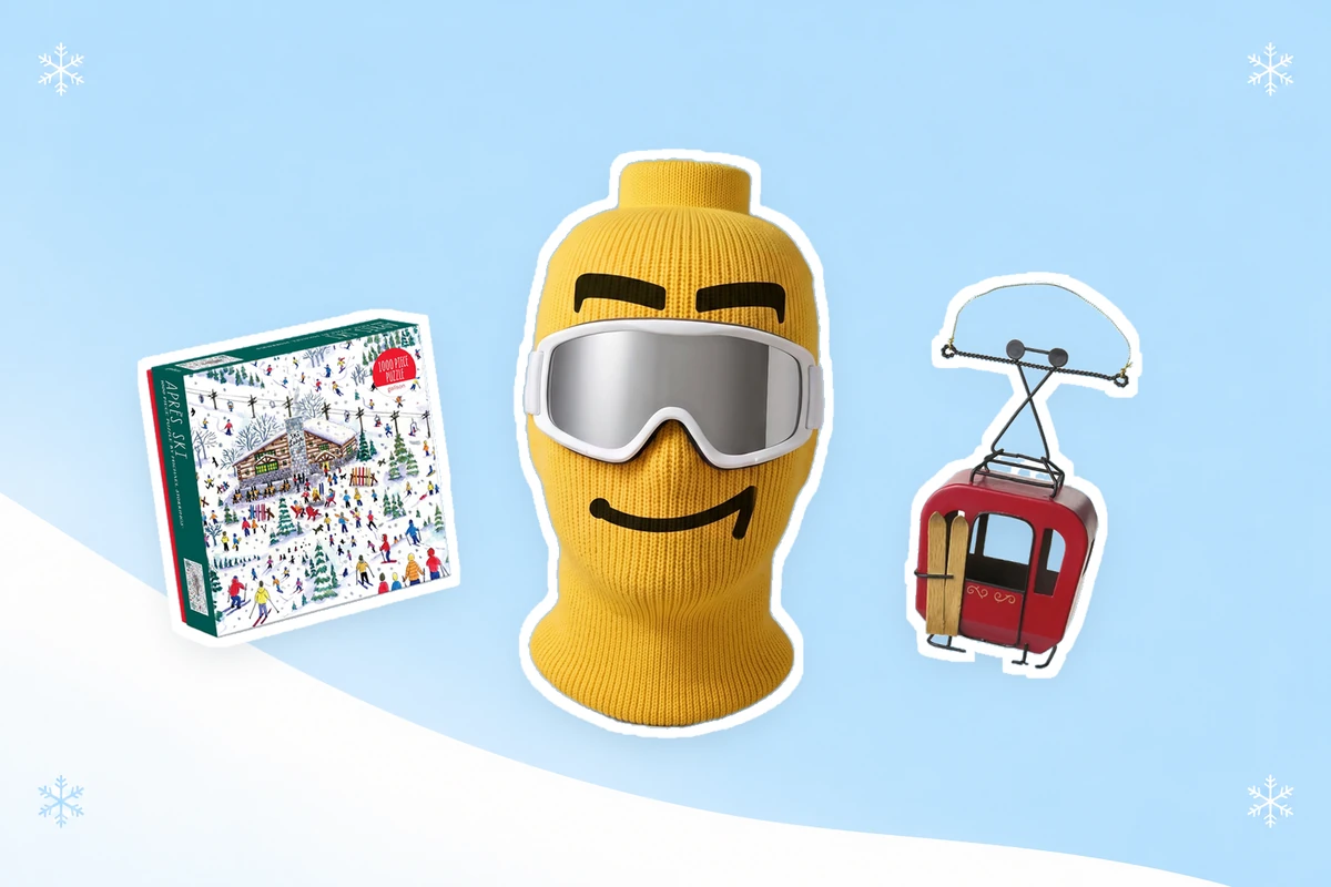 A large yellow Blockhead Smirk ski mask with styling goggles centered between a smaller Après Ski puzzle box and red gondola ornament on an icy blue and white background with delicate snowflakes