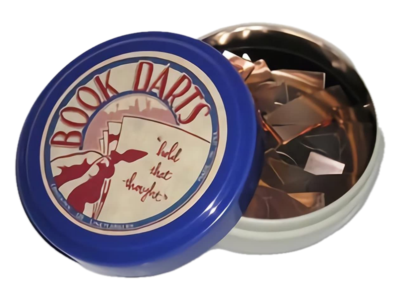 An open tin of mixed-metal Book Darts beside its blue and cream lid, in a retailer photograph